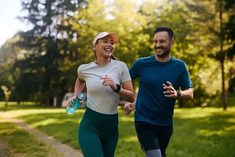 Cheerful athletic couple jogging through park